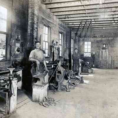 Interior of Lee Smith's blacksmith shop on Biddle St- between Michigan and Park. Smith (in foreground) and assistant Charlie Berger. About 1910.