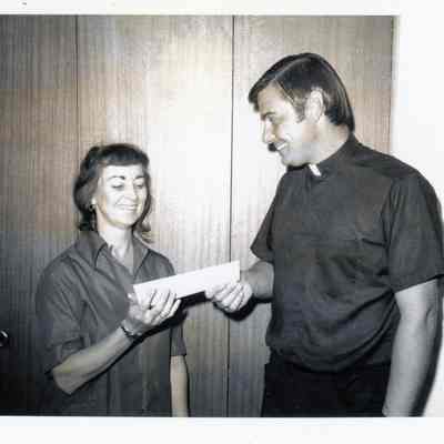 Fr. Sayers presenting bond to Alice Herbst for husband Donald