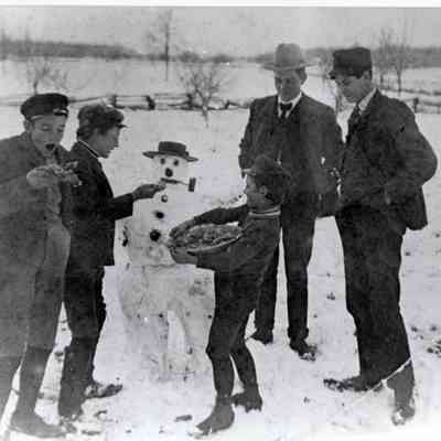 Boys and men making a snowman.
