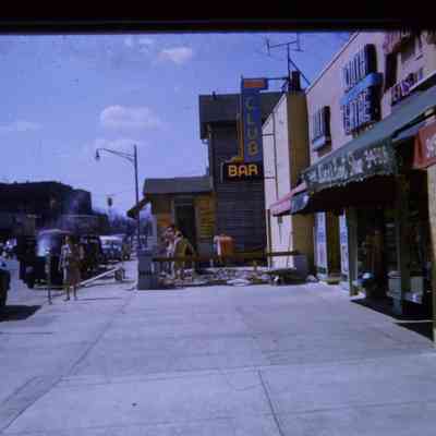 Slide. View West down sidewalk. Club Bar facade has been demolished and cut back for road widening. Derby House is Next