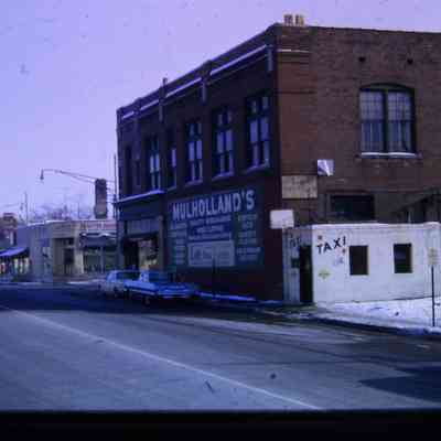 Michigan Ave looking SE. Taxi Stand, Mulhollands, Hoops Block, Gulf, Wrigleys, visible. 1964