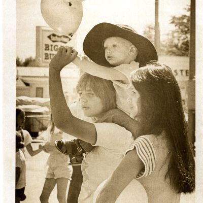 "Going Down" - Young child holding balloons - on the back of one person -
