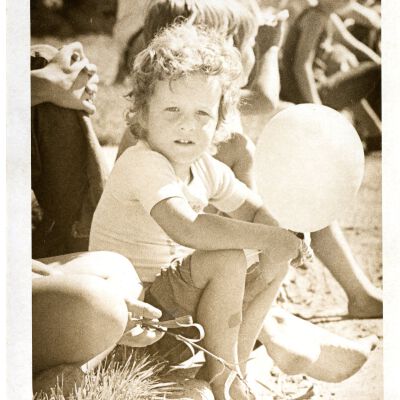 Young child holding balloon - sitting on side of street - looks like parade route