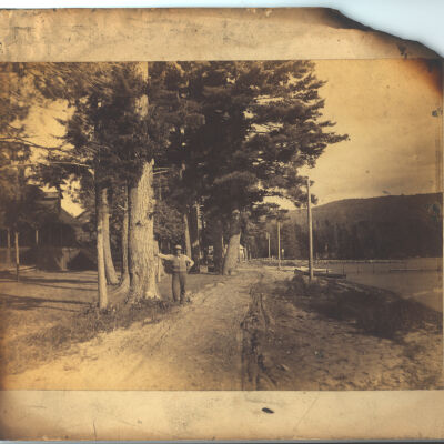 Shore of Meacham Lake, showing cabins, canoe and man standing in foreground
