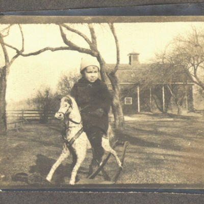 unidentified child on rocking horse in front of Holmes Barn