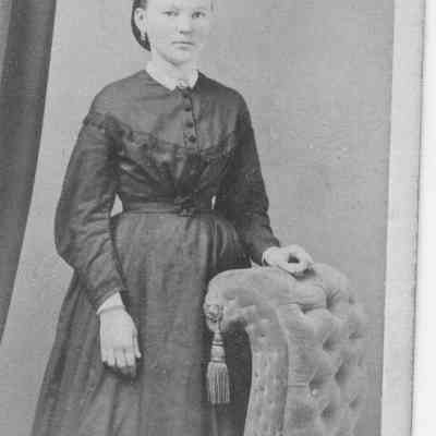 "Maudie", young woman standing by tasseled chair 1890 - 1910