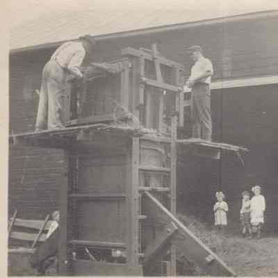 Two men on platform of early hay baling machine