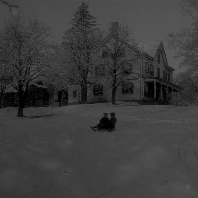 Roscoe and Marion Teator sledding, house in background