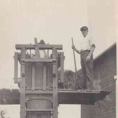 Man standing on a platform next to early hay baling machine