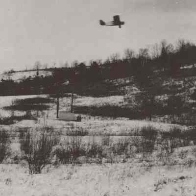 Snowy landscape with airplane flying above it.