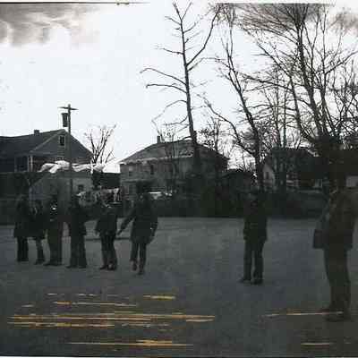 A B/W photograph of several men standing in a parking lot.