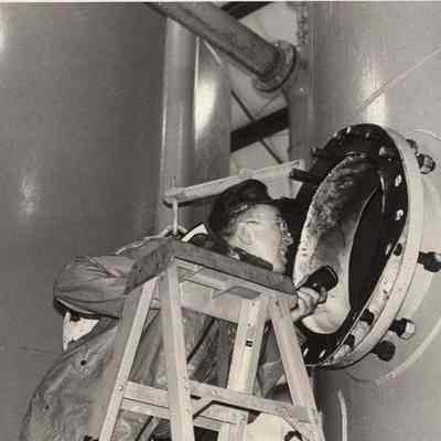 A photo view of a workman checking the inside of a tank. 8/15/1992.