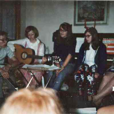 A B/W Polaroid photograph of a group of people sitting around and singing.