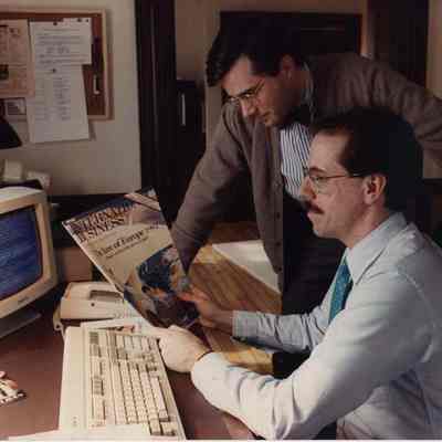 A photo view of 2 men looking at a magazine. 2/26/1990.