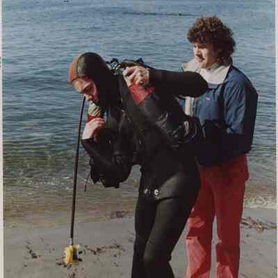 A photo view of a woman putting on diving gear. 4/18/1988.