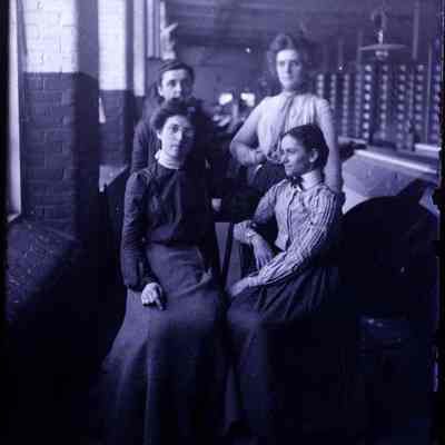 Four women in a factory. Two are sitting and two standing.