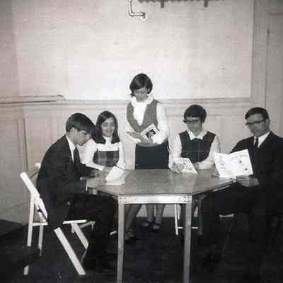 A B/W photograph of 5 people sitting around a table.