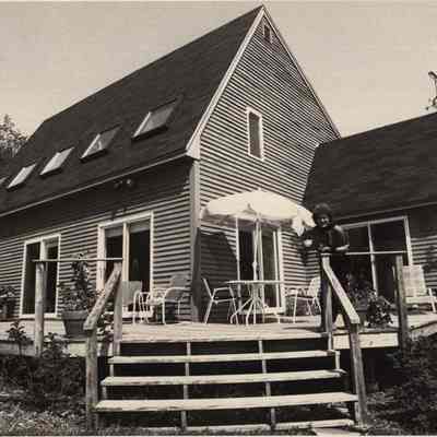 A photo view of a house with a lady out front. 6/8/1992.