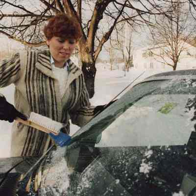 A photo view of a woman scraping ice off her windshield. 1/7/1987.