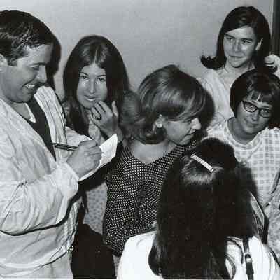 A B/W photograph of a member of the cast of Grease signing autographs.