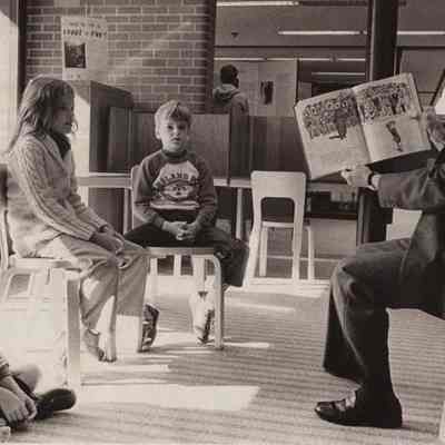 A photo view of a man reading to children.