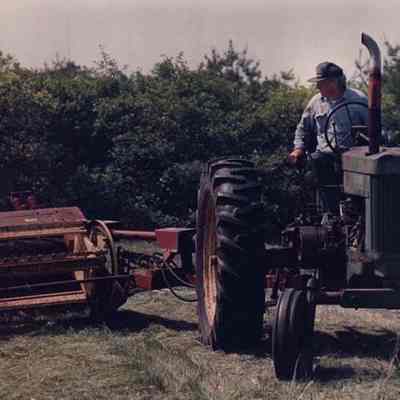 A photo view of a man on a tractor raking hay. 6/16/1988.