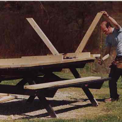A photo view of a carpenter building picnic tables. 6/24/1988.