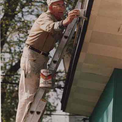 A photo view of a man painting the trim on a house. 6/8/1987.
