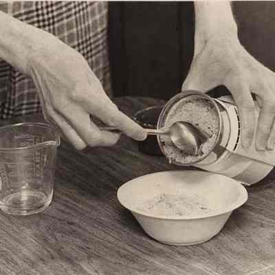 A photo view of Hilda Bloomquist removing nuts from a grinder. 22/22/1982.