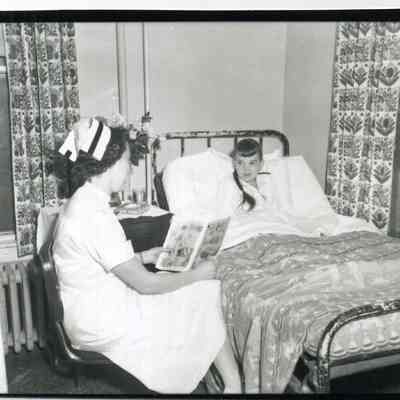 Nurse reading to a young girl in bed in a Brunswick hospital