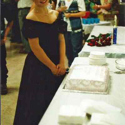 A color photograph of a girl wearing a tiara and cutting a cake.