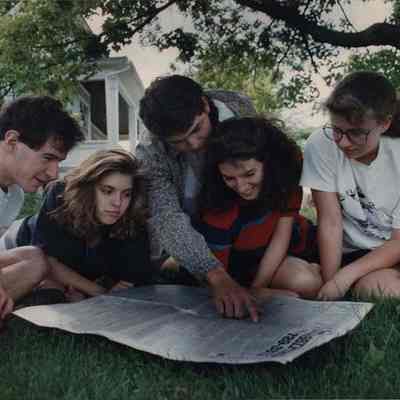 A photo view of a group of young people looking at a newspaper.