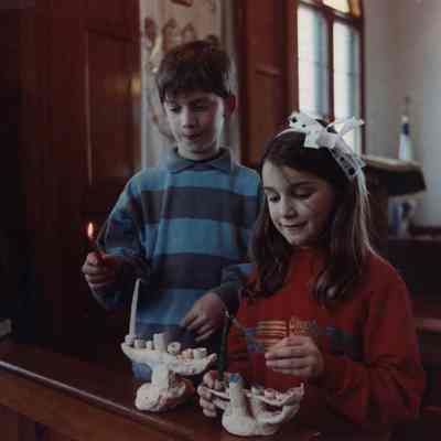 A photo view of two children lighting candles. 12/22/1980.