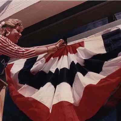A photo view of a woman hanging bunting. 7/13/1989.