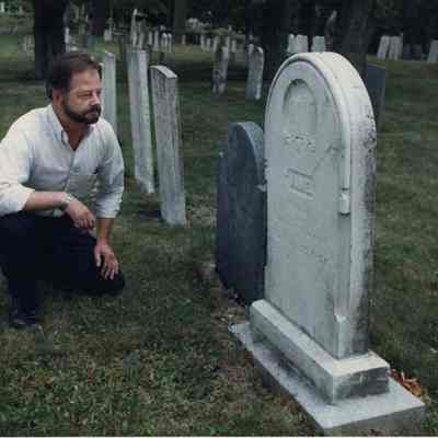 A photo view of a man looking at a gravestone. 8/1/1991.