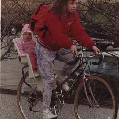A photo view of a woman and baby on a bicycle. 5/2/1988.