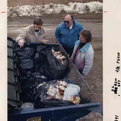 A photo view of three people looking at a pile of trash. 2/28/1990