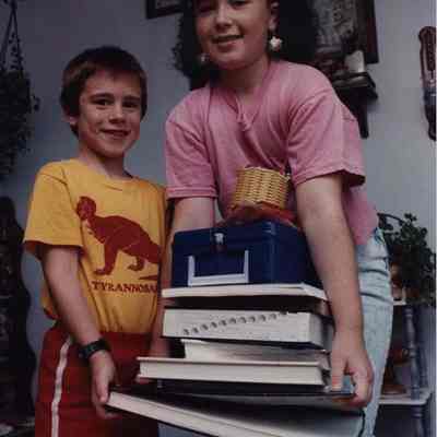 A photo view of 2 children carrying some books.