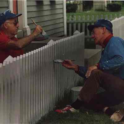 A photo view of two men painting a fence. 6/26/1987.