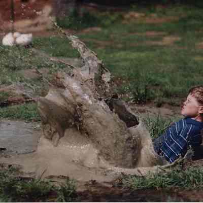 A photo view of a boy splashing in a mud puddle. 5/24/1989.