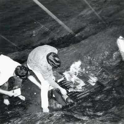 A B/W photograph of two people cooking on a grill.