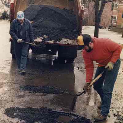 A photo view of workmen patching pot holes. 2/24/1989