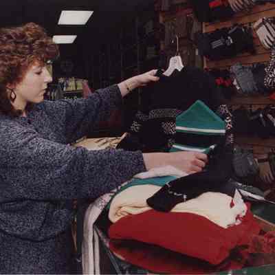 A photo view of a woman looking at sweaters. 12/2/1987.