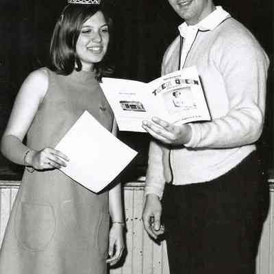 A B/W photograph of a man and woman looking at a Teen Queen booklet.