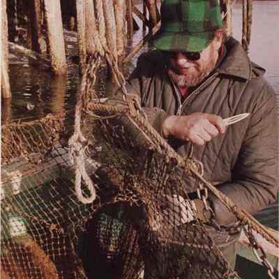 A photo view of a man repairing a fishing net. 3/10/1987.