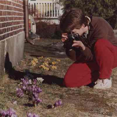 A photo view of a woman taking pictures of some flowers. 3/22/1988.