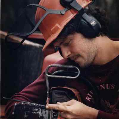 A photo view of Pete Mayo sharpening his chainsaw. 4/5/1989.
