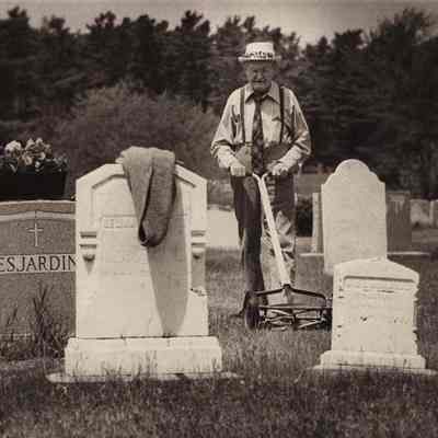 A photo view of a man mowing the grass in a cemetery. 1/29/1979.