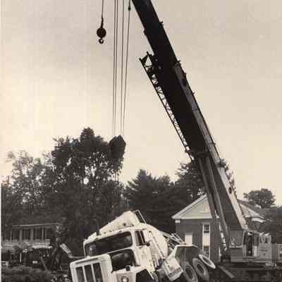 A photo view of a crane setting the cement truck up right.