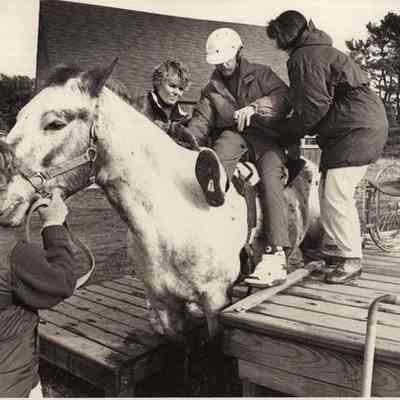 A photo view of a handicap person being helped onto a horse.